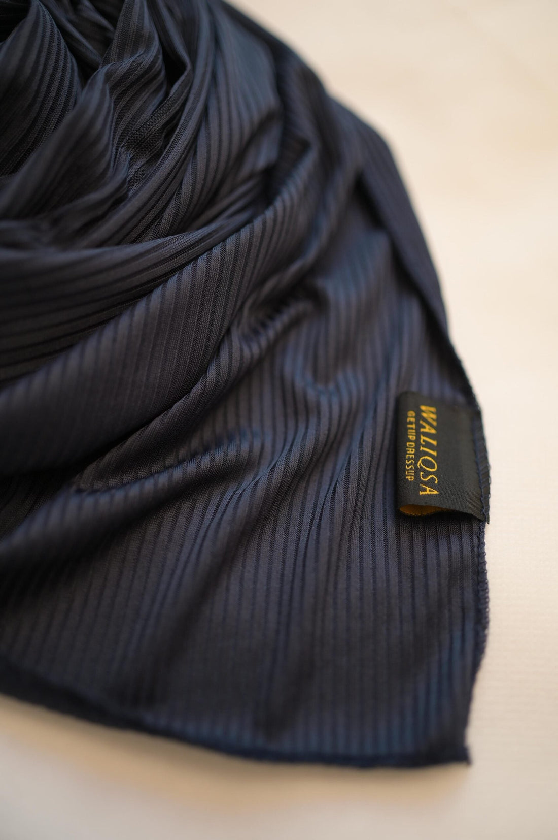 Dark blue jersey hijab folded neatly on white surface with soft texture visible.

