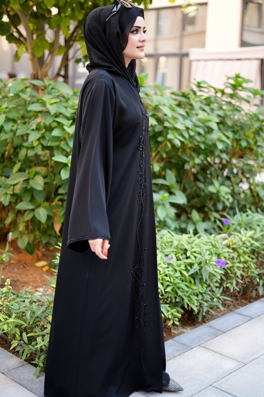 Woman wearing a black abaya with floral embroidery in an outdoor setting.
