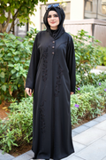 Woman wearing a black abaya with floral embroidery in an outdoor setting.