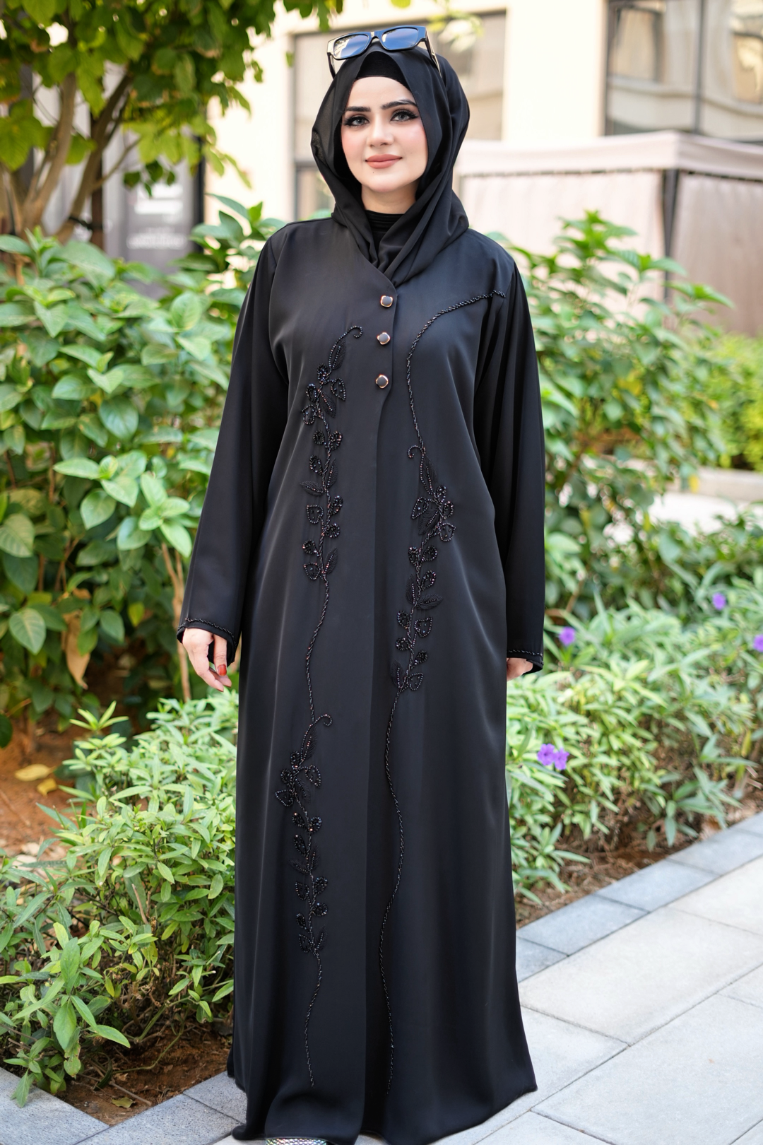 Woman wearing a black abaya with floral embroidery in an outdoor setting.