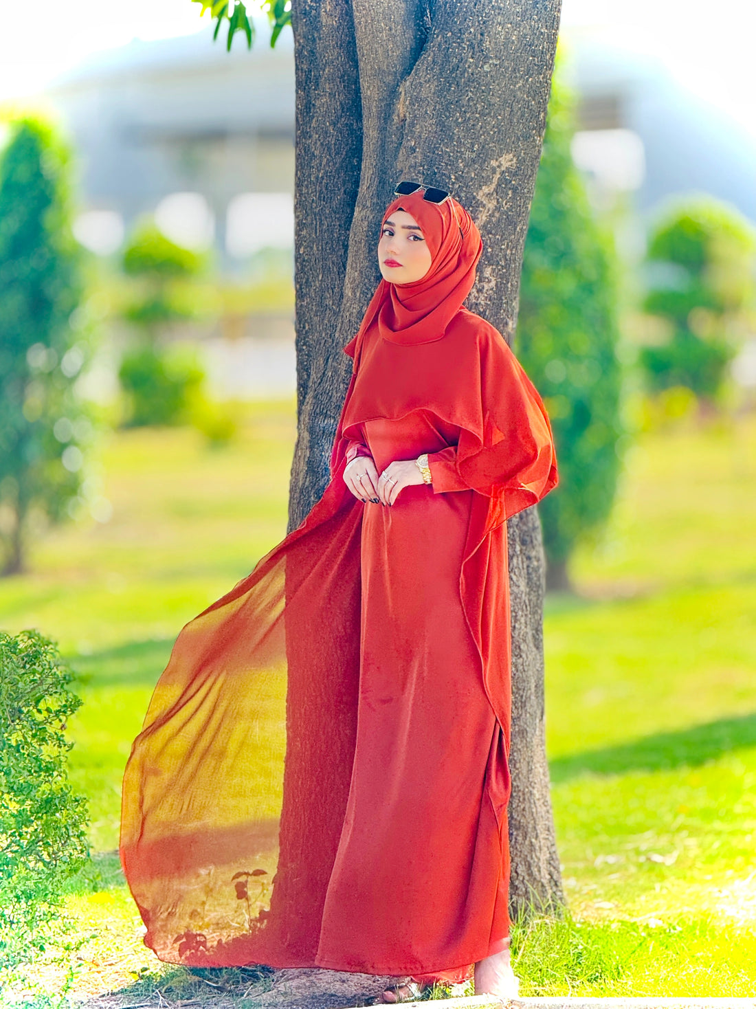 Woman in a orange rust modest outfit standing next to a tree in a park