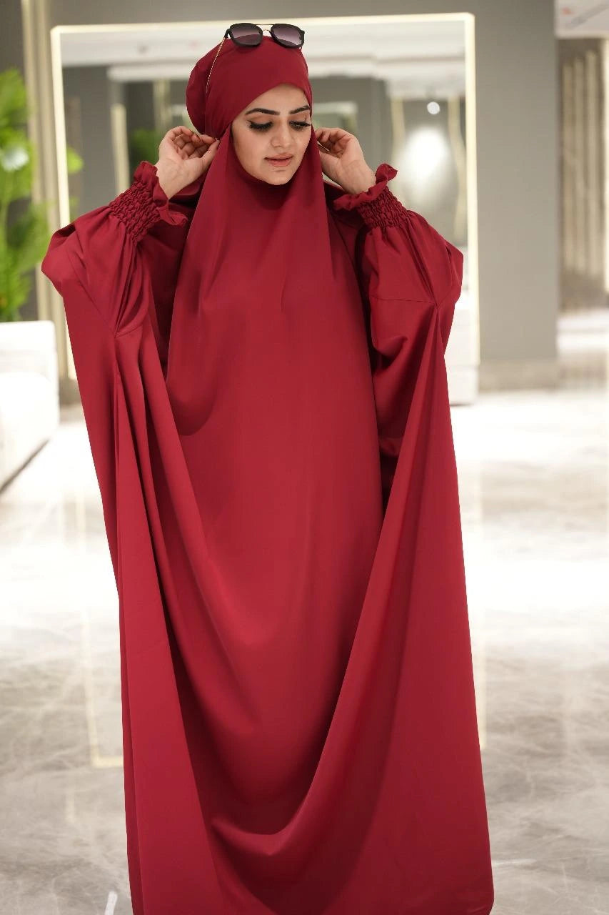 Woman wearing a red abaya with matching headscarf indoors.
